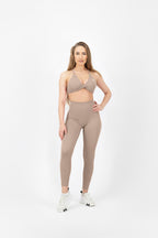 Woman wearing a beige sports bra and leggings set on a white background