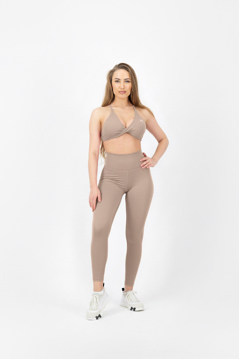 Woman wearing a beige sports bra and leggings set on a white background
