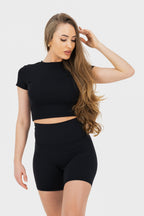 Woman wearing a black crop top and black shorts on a white background